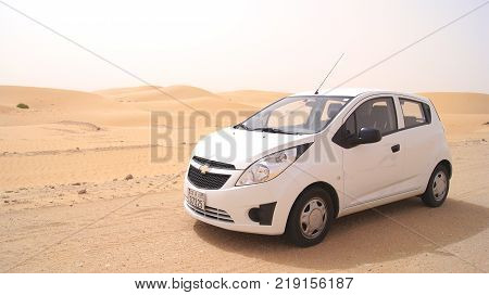 ABU DHABI, UNITED ARAB EMIRATES - APRIL 3rd, 2014: Liwa Desert in Abu Dhabi western region Al Gharbia with a small white car in front.