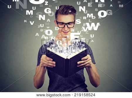 man reading a book with alphabet letters flying up of the book