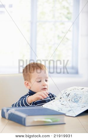 Sladkokyselý dítě studuje encyklopedie doma, sedí u stolu.?