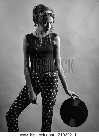 Pretty retro girl young sexy beautiful woman cute melomaniac with stylish hair and pink lips holds black vinyl record with headset in studio on grey background