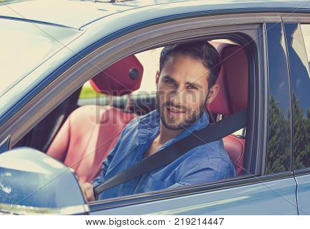 Portrait of handsome guy inside car putting on a safety belt