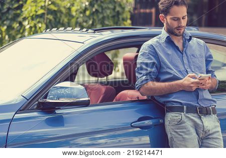 Successful man standing by his car texting on mobile phone