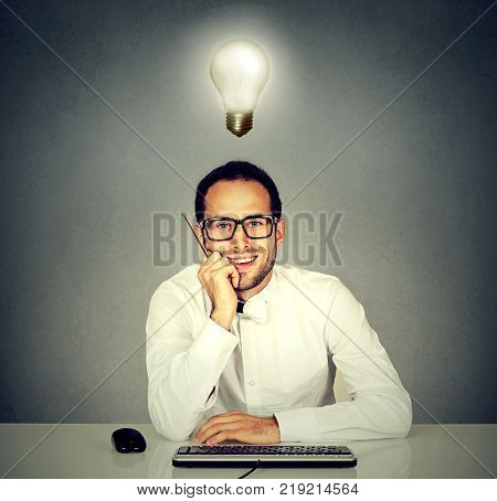 Smiling young handsome man sitting in front of computer keyboard with light bulb over his head
