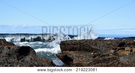 A wave crashing behind rocks at the beach