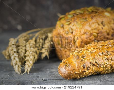 Freshly made baguette and a loaf of bread from wheat flour with ears of wheat on a rustic table. Background of ripe wheat ears.