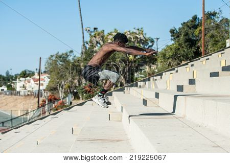 Muscular Jamaican athlete increasing power with plyometric workout at stadium steps.