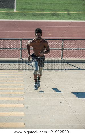 Muscular Jamaican athlete sprinting up plyometric workout at stadium steps in front view.