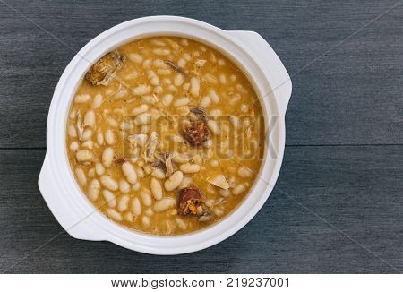 Spanish Fabada in white plate on rustic background with space for copy