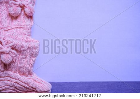 Knitted pink bootees on purple background - Little pink handmade bootees displayed on a blank purple paper with place for text on a purple wooden table. A birth announcement message card idea.