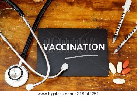 Word VACCINATION written on mini blackboard with stethoscope, syringes and medicine