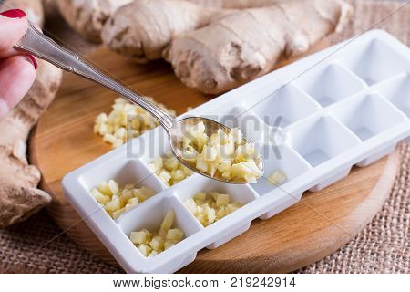 Pieces of ginger in a container for freezing ice cubes on a board on a wooden table