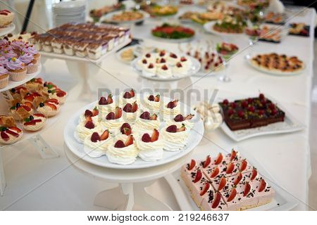 Restaurant catering table full of different types of desserts: creamy pieces of cakes and souffle, secorated with strawberry and chocolate.