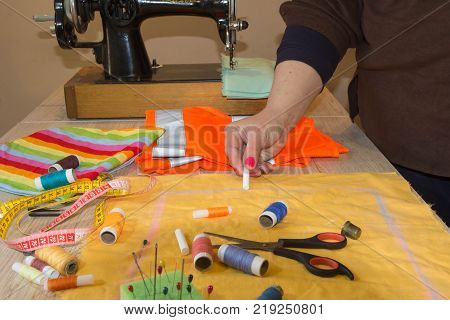 woman's hands drawing a pattern on bright material at her workplace in a tailor shop. Clothes designer at work in her office