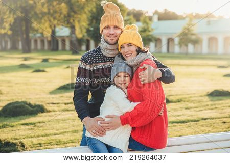 Outdoor portrait of beautiful smiling woman handsome man and their little cute daughter stand together against ancient bilduing in park wear warn knitted clothes have interesting excursion