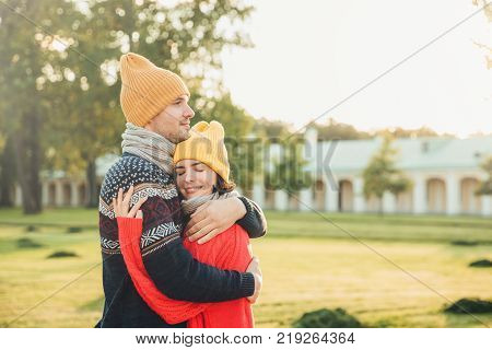 People and closeness concept. Young couple in love have date embrace each other feel support being alone in park have perfect relationships. Handsome man in warm sweater and hat hugs girlfriend