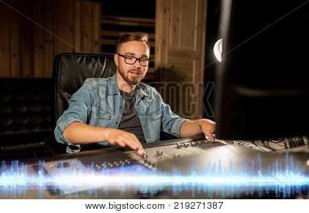 music, technology, people and equipment concept - sound engineer with mixing console recording track at studio