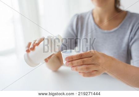 healthcare, people and medicine concept - woman pouring medication or antipyretic syrup from bottle to cup