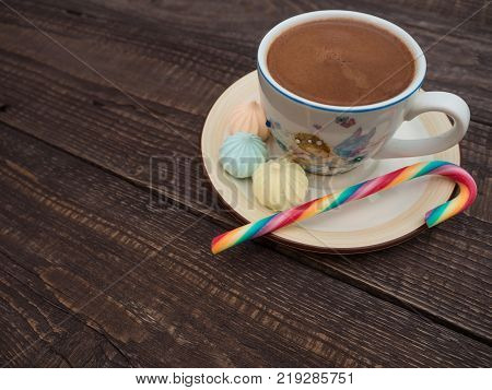 Freshly brewed cocoa and colorful biseza with candy on an old wooden table