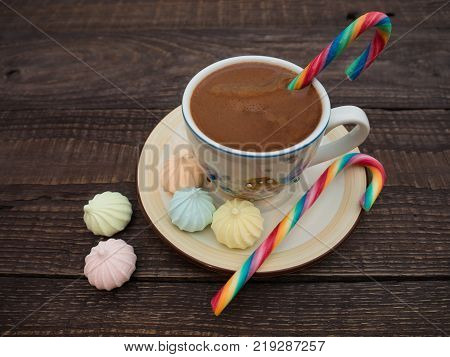 Freshly brewed cocoa and colorful biseza with candy on an old wooden table