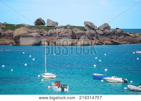 Beautiful seascape with white andblue sea and boat and buoy floating on big dark gray brown stones blue sky seaside in Trègastel France Europe.