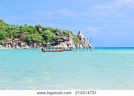 Beautiful seascape in summer season with aqua and blue sea with people sit on long tail boats big rock and coconut trees near small port bugalow on coastside white clouds and blue sky.