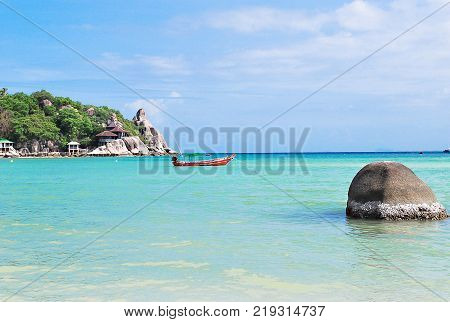 Beautiful seascape in summer season with rock on the beach aqua and blue sea with boat floating on big rock and coconut trees near small port bugalow on coastside white clouds and blue sky.