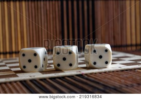 Stack of three white plastic dices on brown wooden board background. Six sides cube with black dots. Number 5