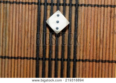 One white plastic dice on brown wooden board background. Six sides cube with black dots. Number 3