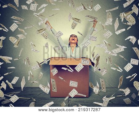Successful woman coming out from a box under money rain. Financial success concept