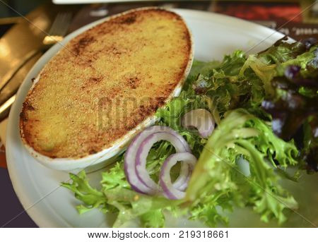 Gratin with fish and cheese with green salad and onions