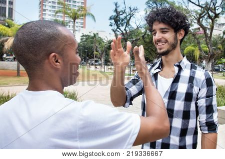 Hipster man giving high five to african american friend outdoors in the city in the summer