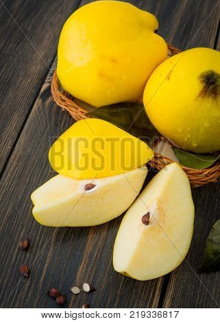 A wicker basket of yellow quince or queen apple autumn fruits, sliced lobules and seeds on black rustic wooden background close-up