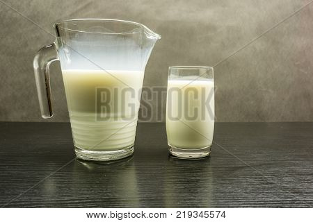 Milk in a jug and a glass on a wooden table.