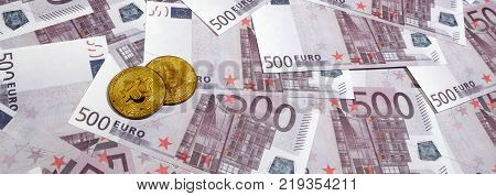 Bitcoins over pile of five hundred euro banknotes. Traditional money versus cryptocurrency concept. Gold coin above 500 euro bills. Close up