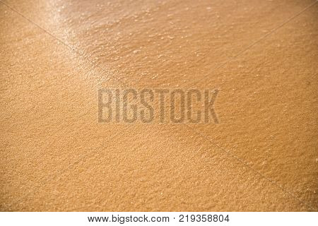 Background. A close up of a wave runs over a sandy beach