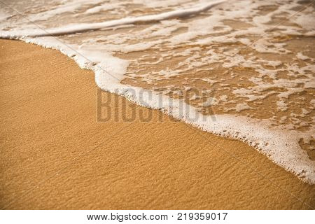 Background. A close up of a wave runs over a sandy beach