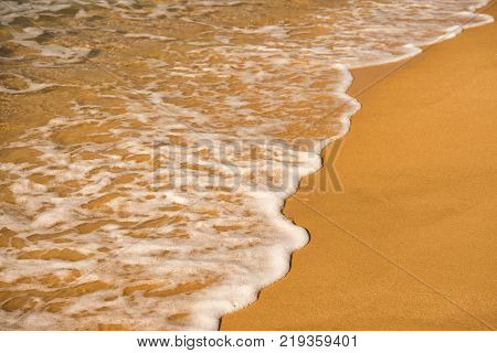 Background. A close-up of a wave runs over a sandy beach