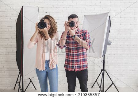 portrait of young man and woman taking photo with professional camera in studio with lighting at the background