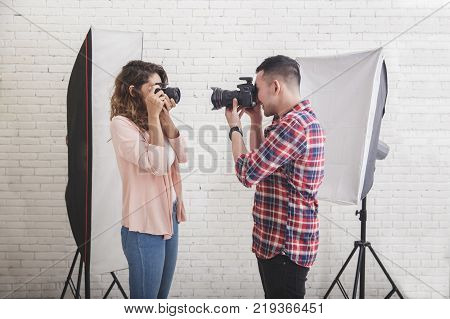 portrait of two young photogaphers taking photo of each other in professionally equipped studio