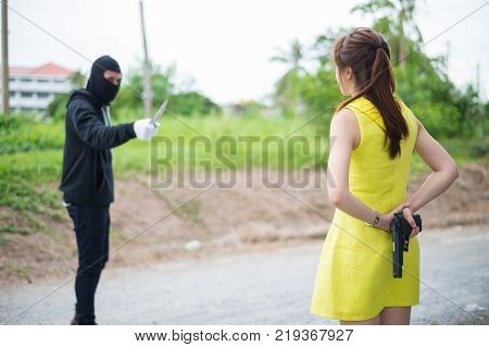 Criminal or Bandit wear black mask use knife point to woman trying to rob money and hurting her but the woman but women hid their guns behin concept of winner fighting usurpation