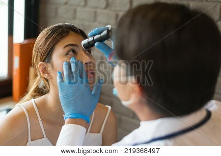 The doctor wear white coat shines a flashlight at the eyes of a female patient at a clinic. Concept of Healthcare Medical treatment examination