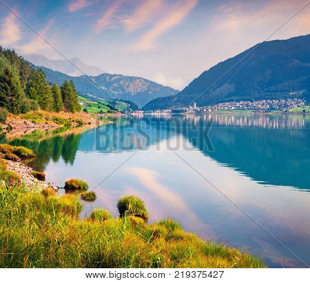 Colorful summer sunrise on Resia (Reschensee) lake. Resia village in the morning mist Province of Bolzano - South Tyro Italy Europe. Artistic style post processed photo.
