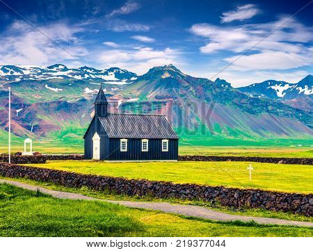 Black wooden Budakirkja church at Saefellsnes. Dramatic summer morning with field of fresh green grass on Snafellsnes peninsula western Iceland Europe. Artistic style post processed photo.
