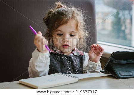 Little kid girl writing or drawing with pen in scetch book.