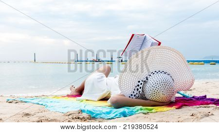 The Asian Girl Reads Alone At The Beach, Lonely, Wearing A White Hat, Wearing A Ukulele Over Her In