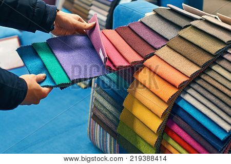 Young woman is making her decision while choosing a color of a fabric from a huge variety in a shop