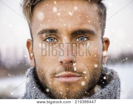 Headshot of handsome young man outdoor in winter fashion, wearing turtleneck sweater duriing snowfall