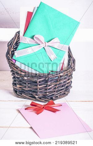 Basket with colorful envelopes and paper note - Wicker basket full of multicolored letters tied together with ribbon and a blank message card with a red bow on a white wooden table.