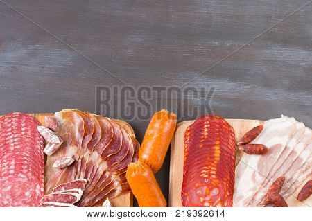 Bordure of different Spanish appetizer, like fuet, jamon, chorizo, bacon and lomo embuchado on a black wooden background.