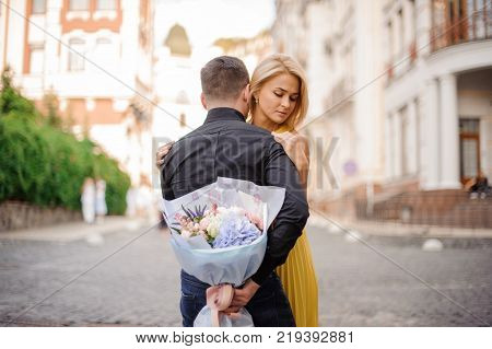 pretty blonde girl with a bouquet of flowers including roses astilba carnations and hydrange hugs her boyfriend